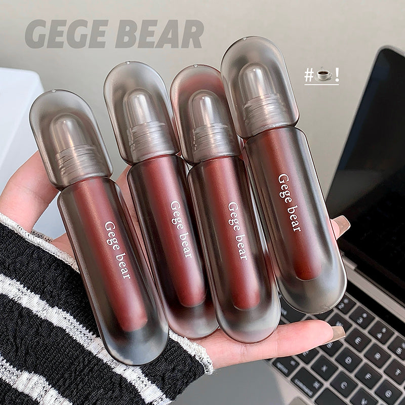 Five GEGE BEAR lip glosses held in a hand with a blurred laptop background
