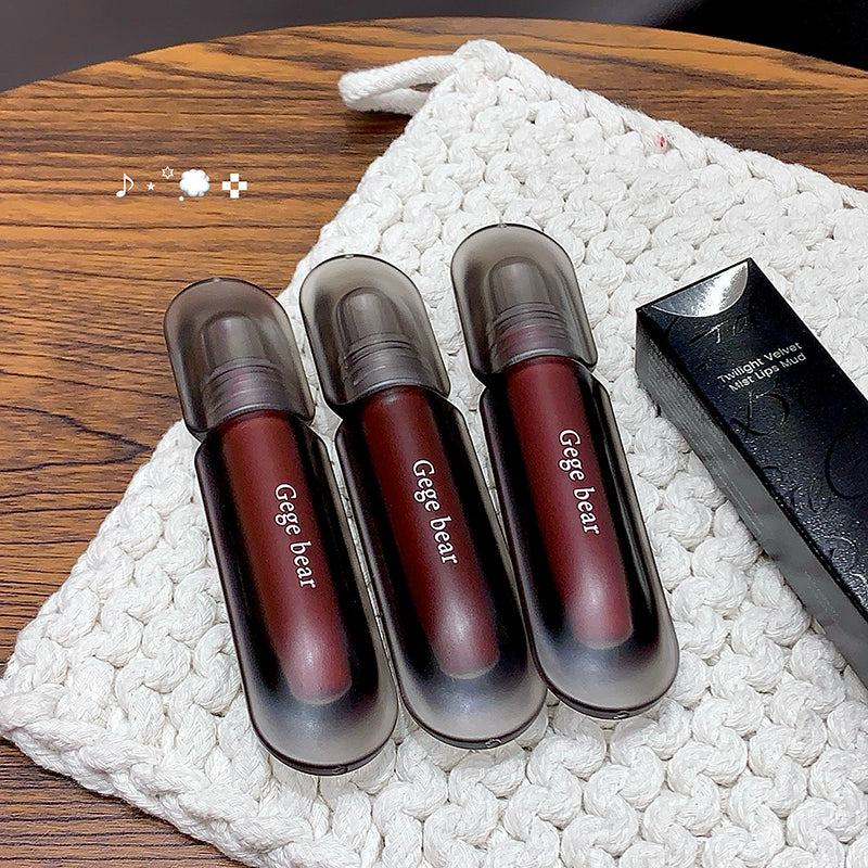 Three Gege bear lip glosses on a textured white surface with a wooden background.