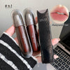 Two lip products with packaging held by a hand, laptop in the background