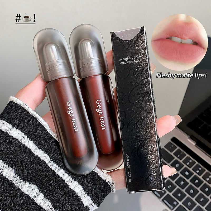Two lip products with packaging held by a hand, laptop in the background