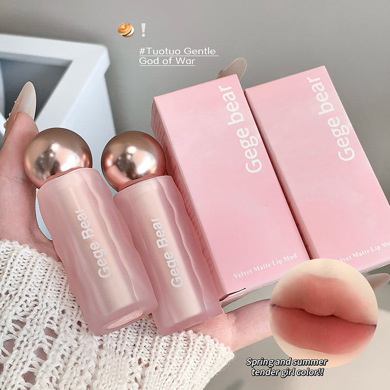 Two pink lip products with gold caps and 'Gege Bear' packaging on a textured surface.