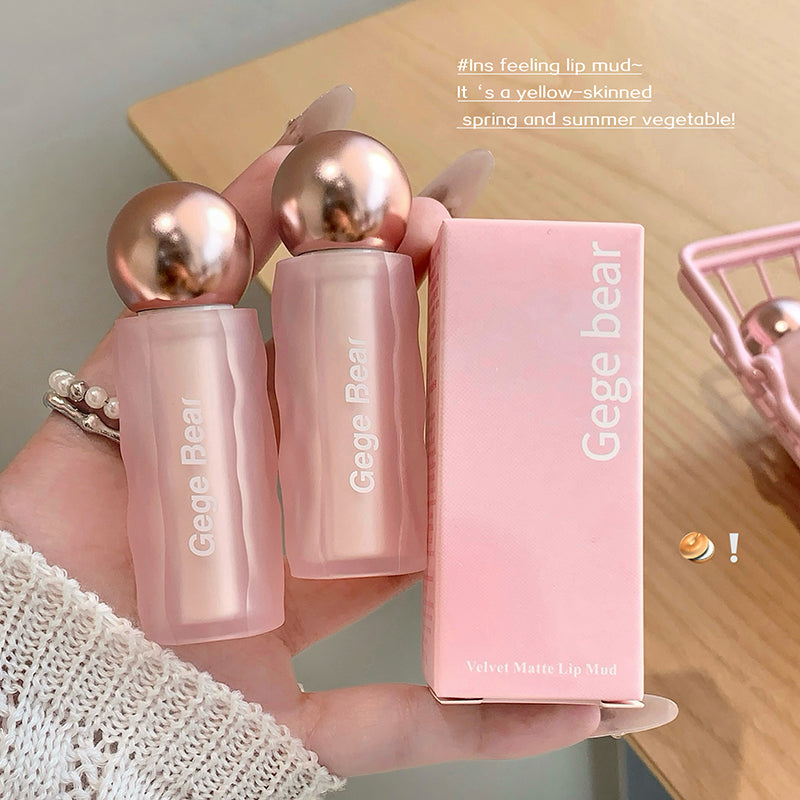 Pink 'Gege Bear' lip mud with packaging held by a hand on a wooden surface.