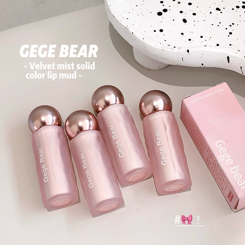 Four pink lip mud products with metallic caps on a light surface, next to their packaging.