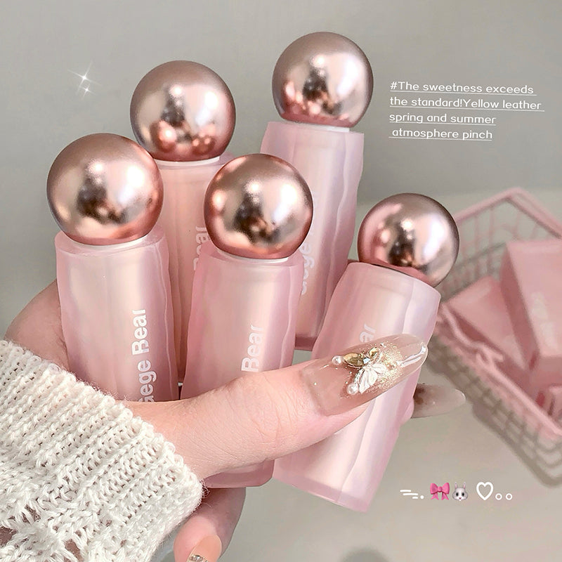 Pink lip balms with rose gold caps held by a hand against a neutral background