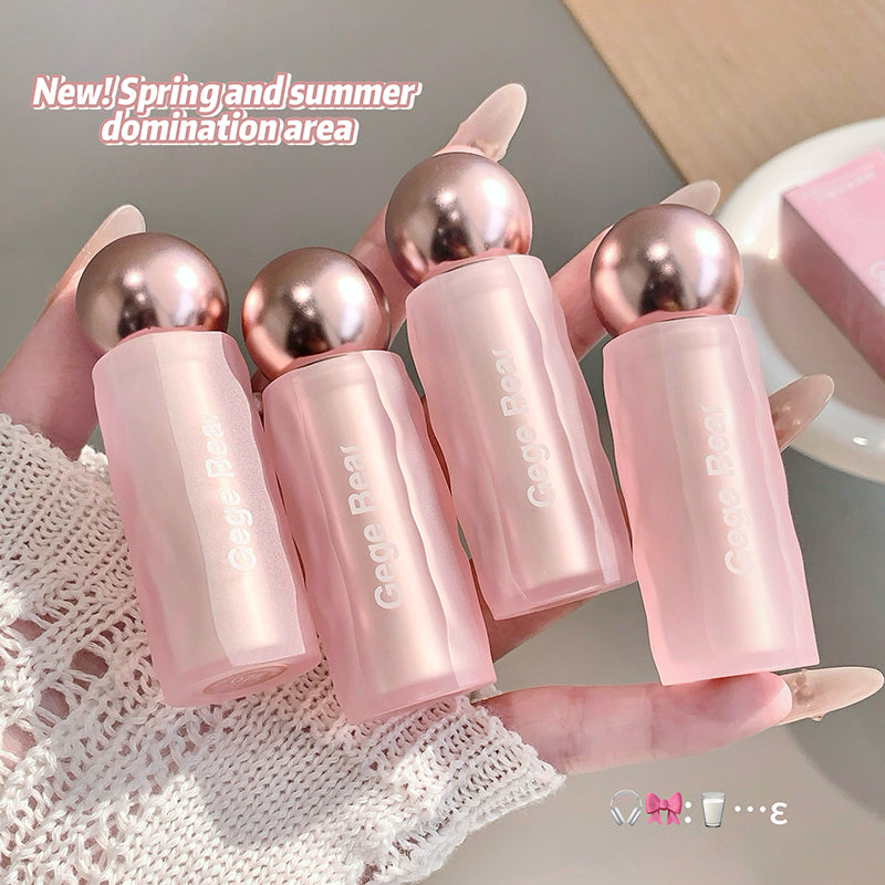 Set of pink lip balms with metallic tops held by a hand on a textured surface.