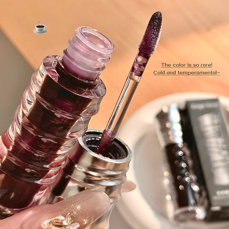 Close-up of a lip gloss with applicator and text on a blurred background