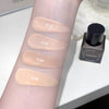 Four swatches of cosmetic product on a person's arm with labeled numbers, next to a bottle.