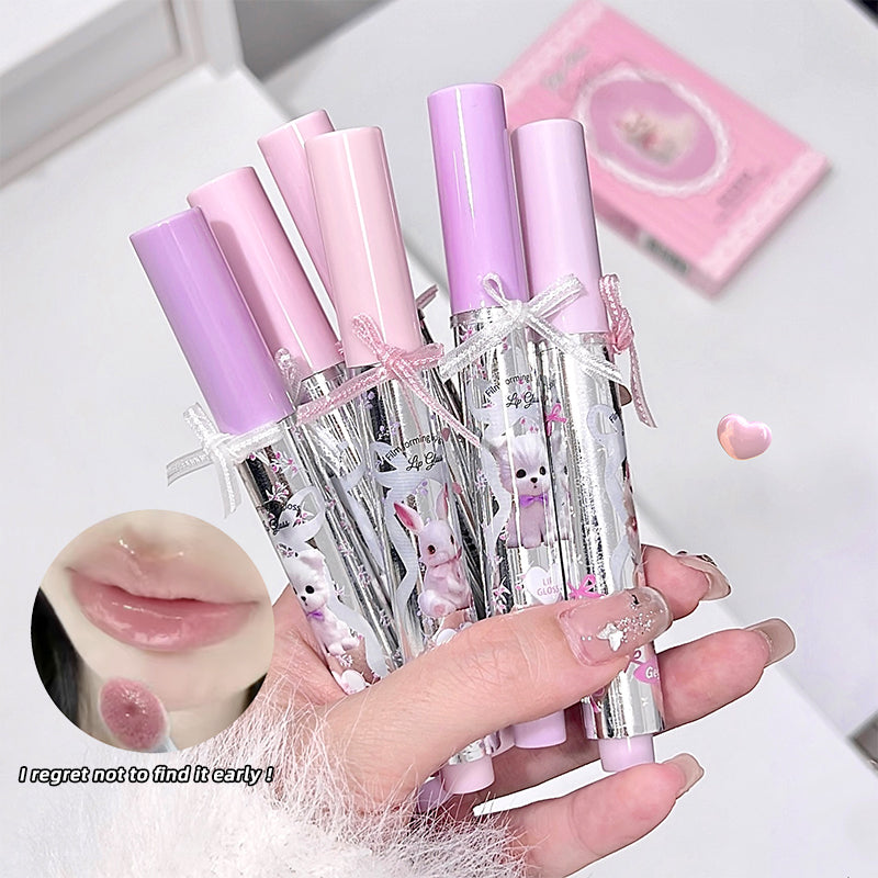 Set of pink lip glosses with rabbit designs held by a hand on a light background.