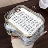Stack of false eyelashes in a clear plastic case on a wooden surface.