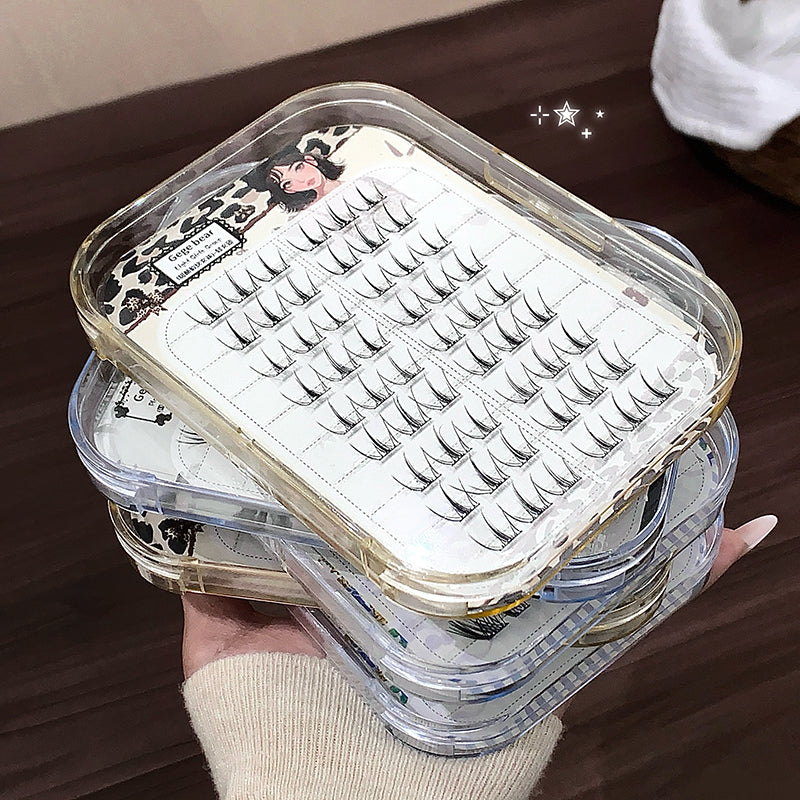 Stack of false eyelashes in a clear plastic case on a wooden surface.