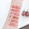 Lip gloss swatches on a person's arm with labeled shades, next to lip gloss bottles.