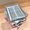 Stack of false eyelash boxes with a clear lid showing eyelashes on a wooden surface.