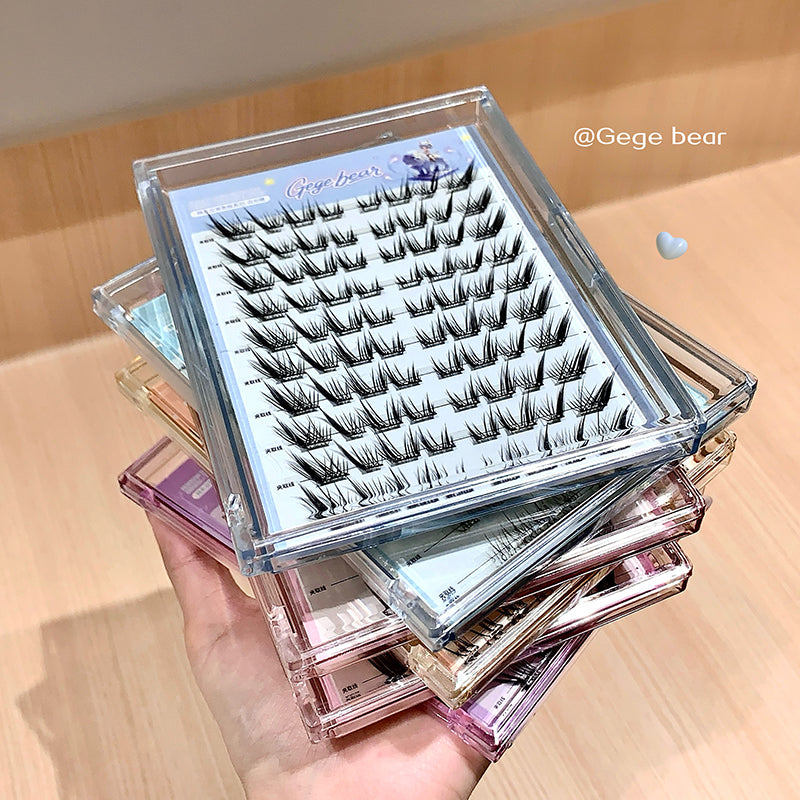 Stack of false eyelash boxes with a clear lid showing eyelashes on a wooden surface.