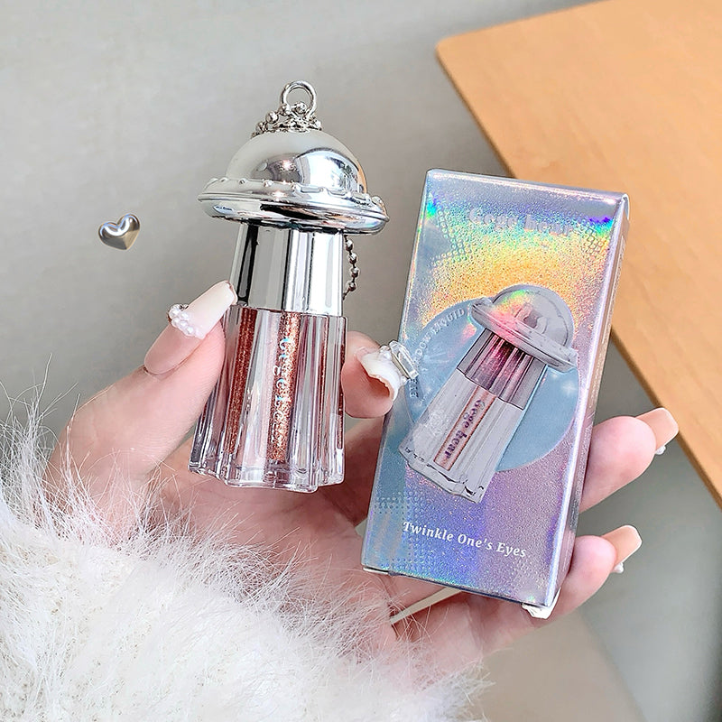 Hand holding a silver and clear cosmetic product with packaging labeled 'Twinkle One's Eyes' against a neutral background.