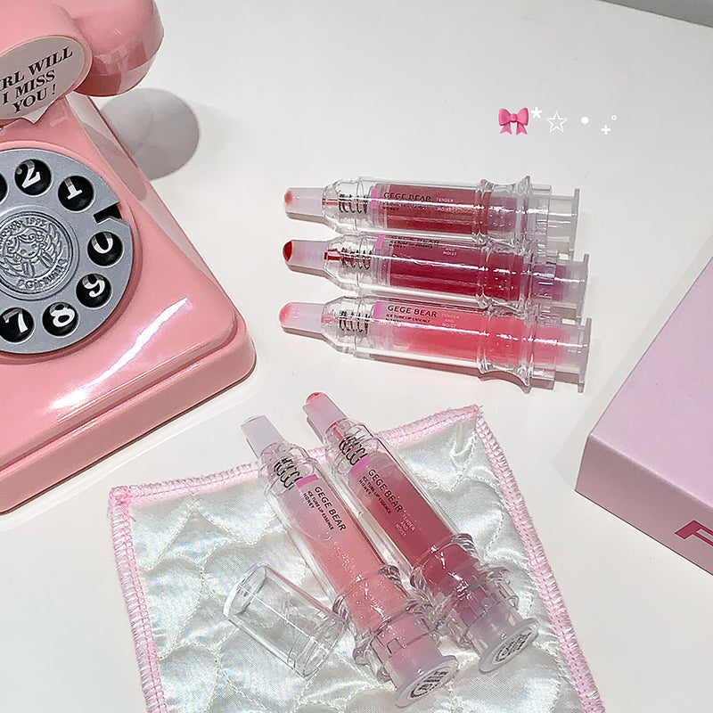 Pink vintage phone and lip glosses on a white surface