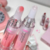 Two pink lip serum bottles with white caps held by a hand, with a blurred background.