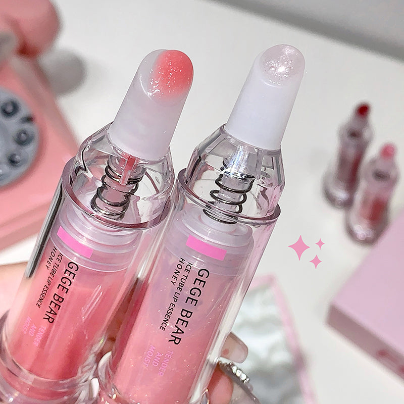 Two pink lip serum bottles with white caps held by a hand, with a blurred background.