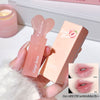 Pink lip balm with heart-shaped cap held by a hand, next to its packaging on a white surface.