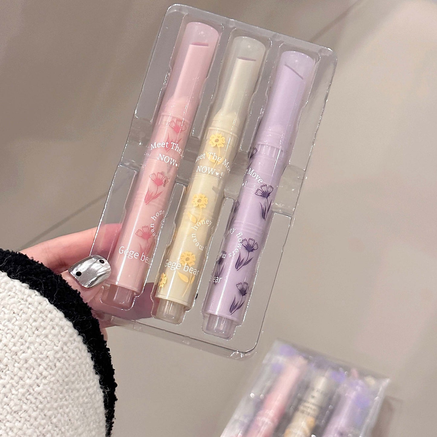 Set of three pastel-colored lip balms in a clear packaging on a neutral background.