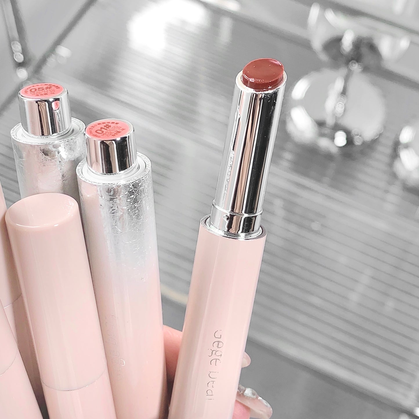 Set of lipsticks with pink and silver caps on a reflective surface