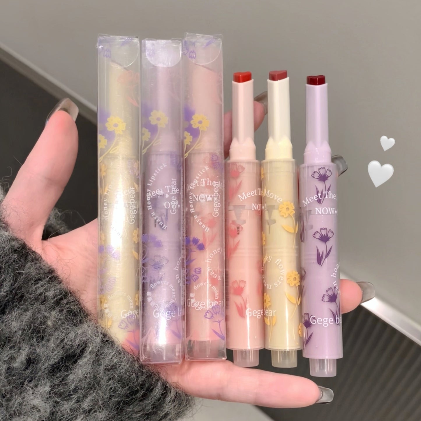 Hand holding six floral-themed lip balms with their packaging against a neutral background