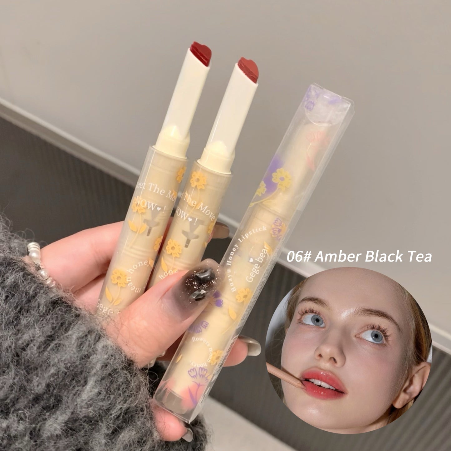 Two lipsticks with floral packaging held by a person, with a blurred face in the corner.