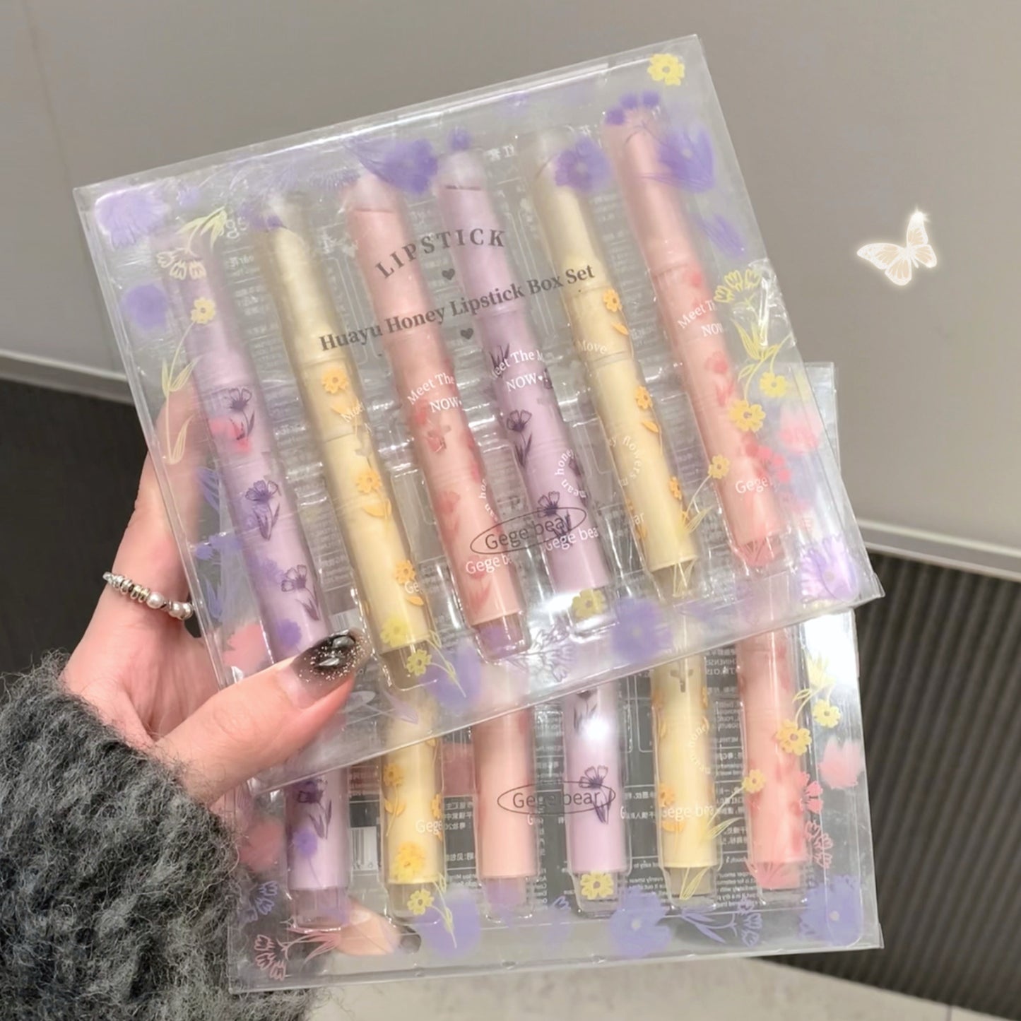 Set of lipsticks in a clear packaging box held by a person.