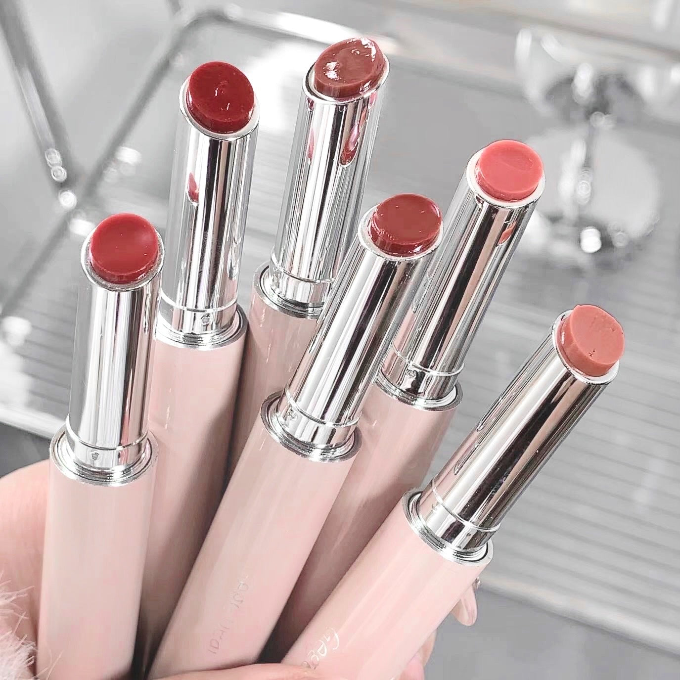 Set of pink lipsticks with silver caps on a reflective surface