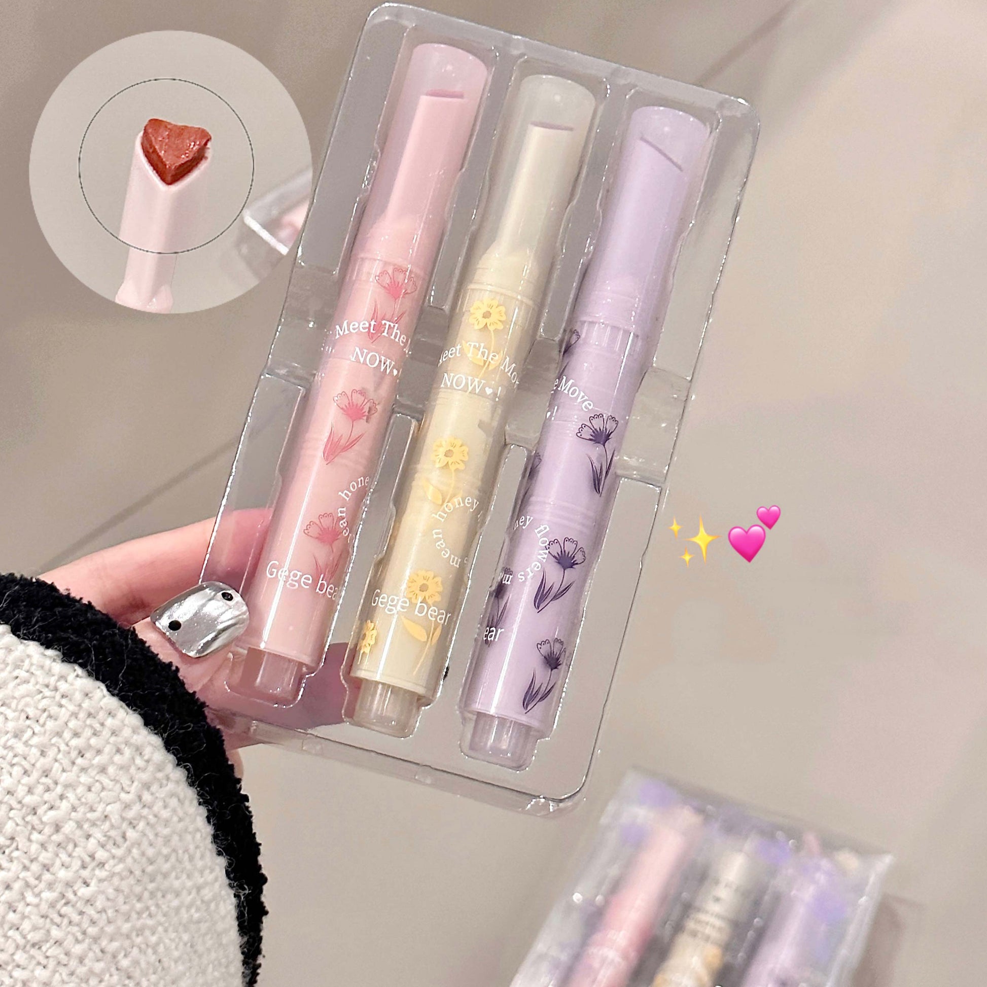 Set of three pastel-colored lip balms in a clear packaging case held by a person.