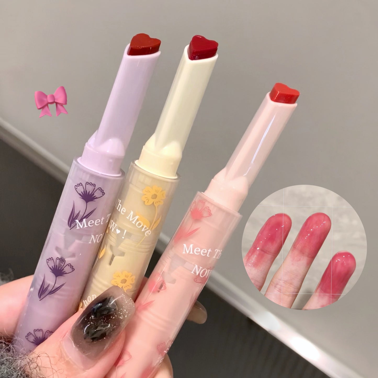 Three lip glosses with floral designs on a neutral background