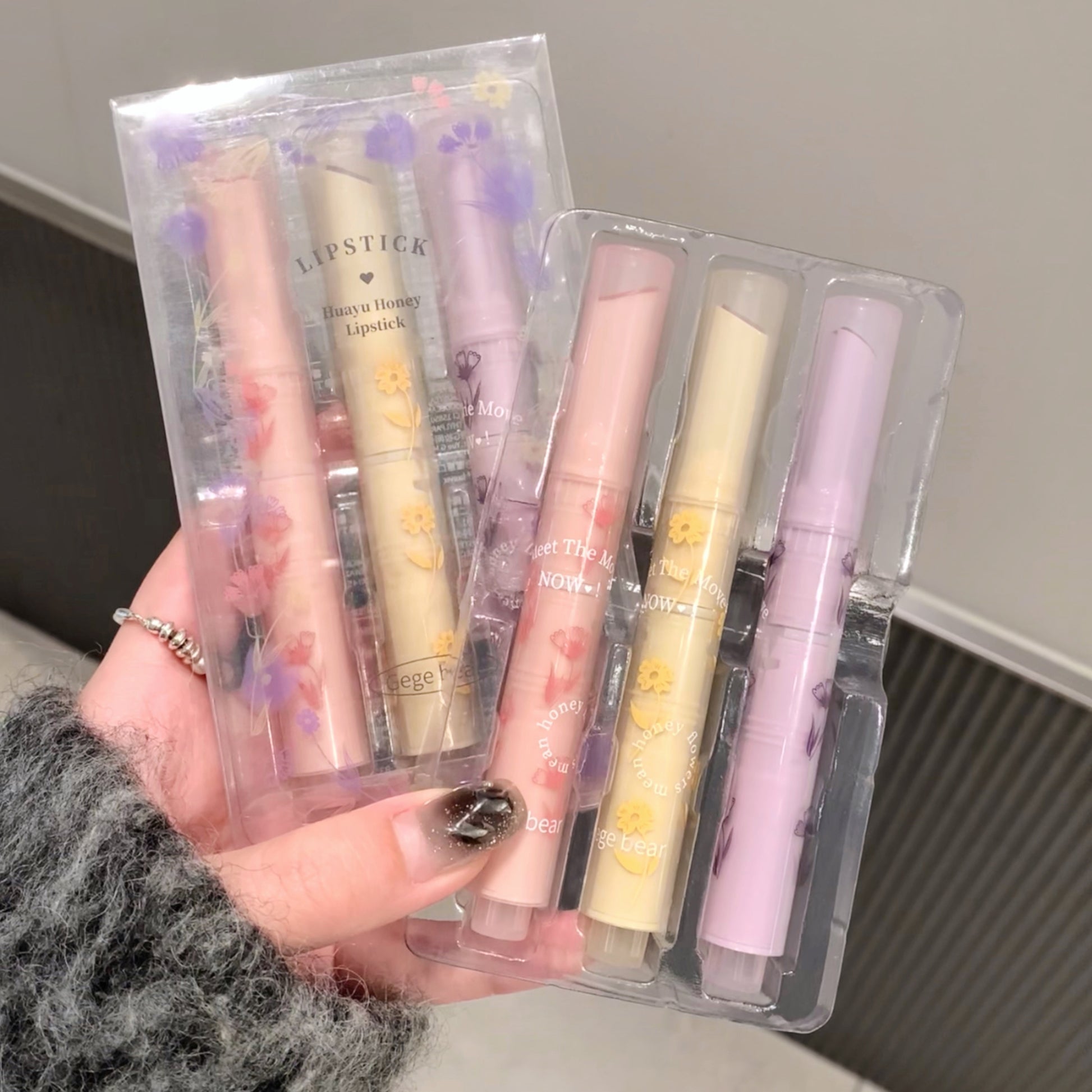 Set of pastel-colored lipsticks in clear packaging held by a person.