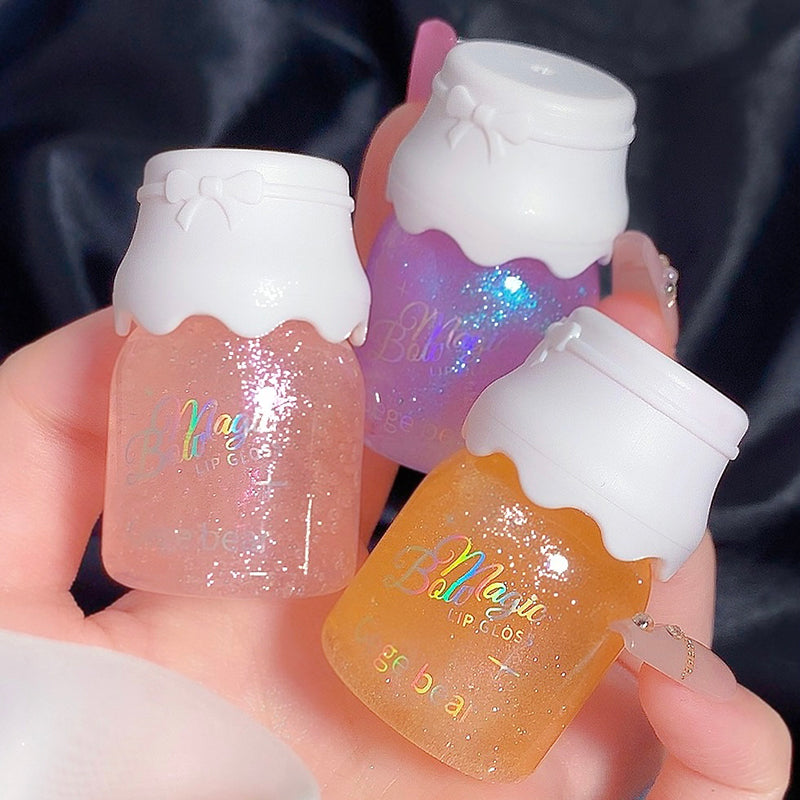 Three small bottles of 'Bella' lip gloss held in a hand against a dark background.