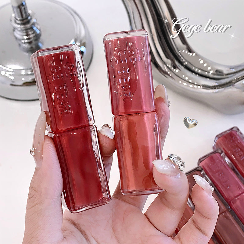 Two red nail polishes held by a hand with a blurred mirror background