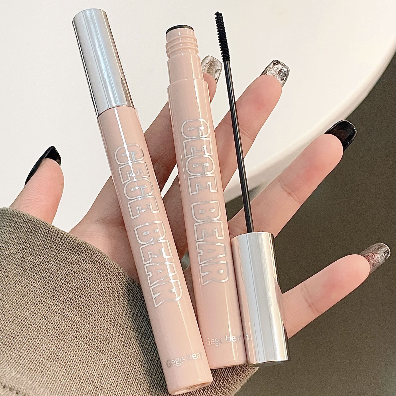 Makeup products including a mascara wand and two lip products held by a hand.