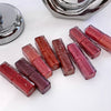 Set of lip glosses in various shades on a white surface with a mirror in the background.