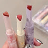 Three lip glosses with heart-shaped caps held by a hand against a neutral background.