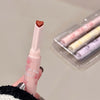 Pink lip gloss with heart-shaped cap held by a hand, with more lip glosses in the background.
