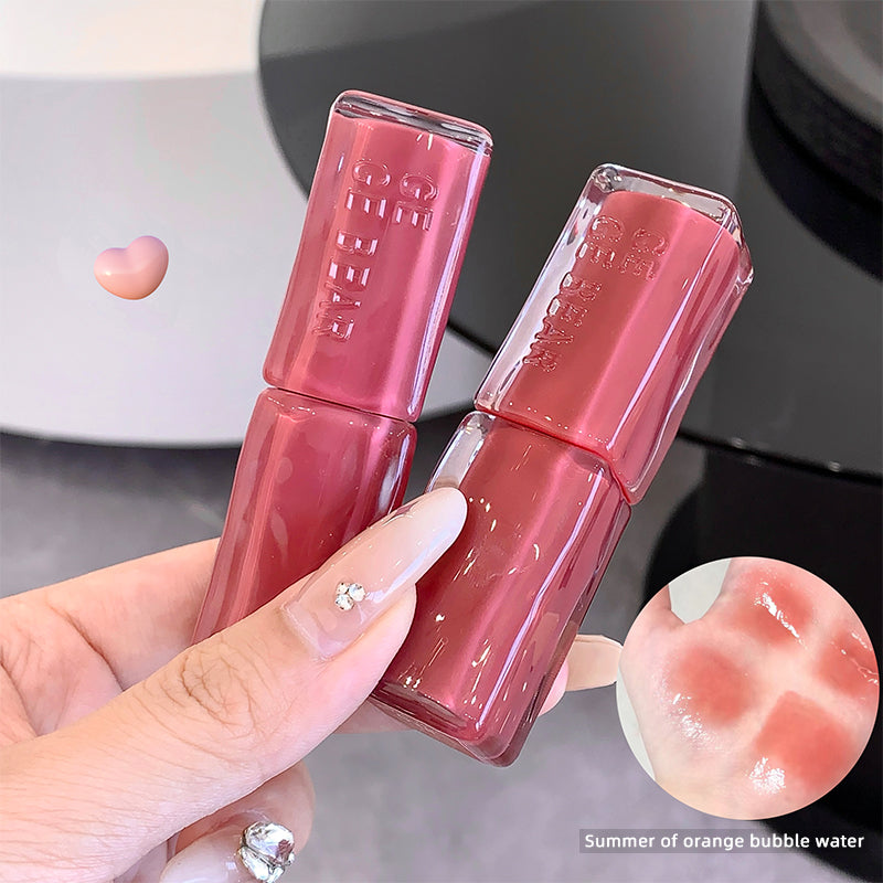 Two pink lip glosses held by a hand with a close-up of the product texture on a blurred background.