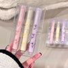 Set of three lip glosses in clear packaging held by a person.