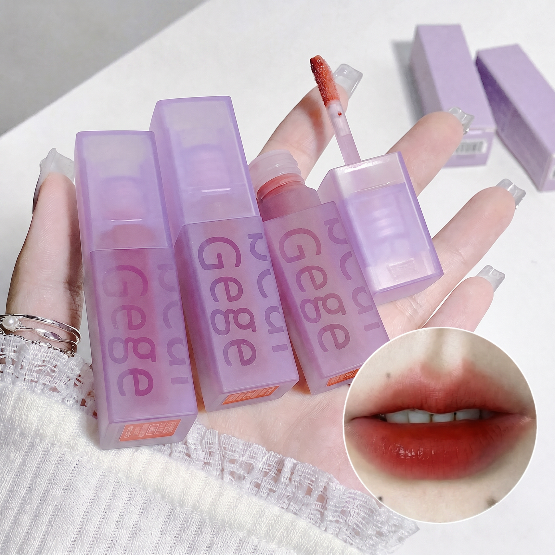 Purple lip gloss with 'GEGE' branding on a white background, showing a close-up of lips wearing the gloss.